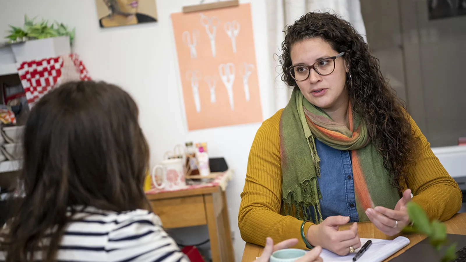 Mary Rodriguez sits across a table speaking to a women holding a coffee mug