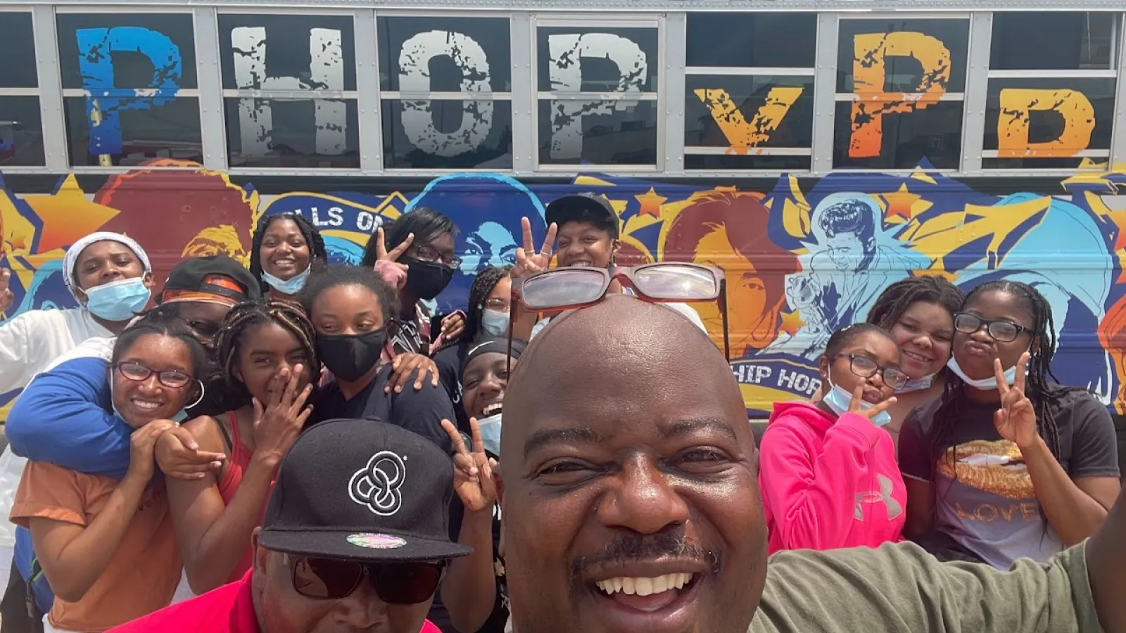 Dr. Will Patterson stands atop a crowd posing in front of the Hip Hop Xpress Double Dutch Boom Bus