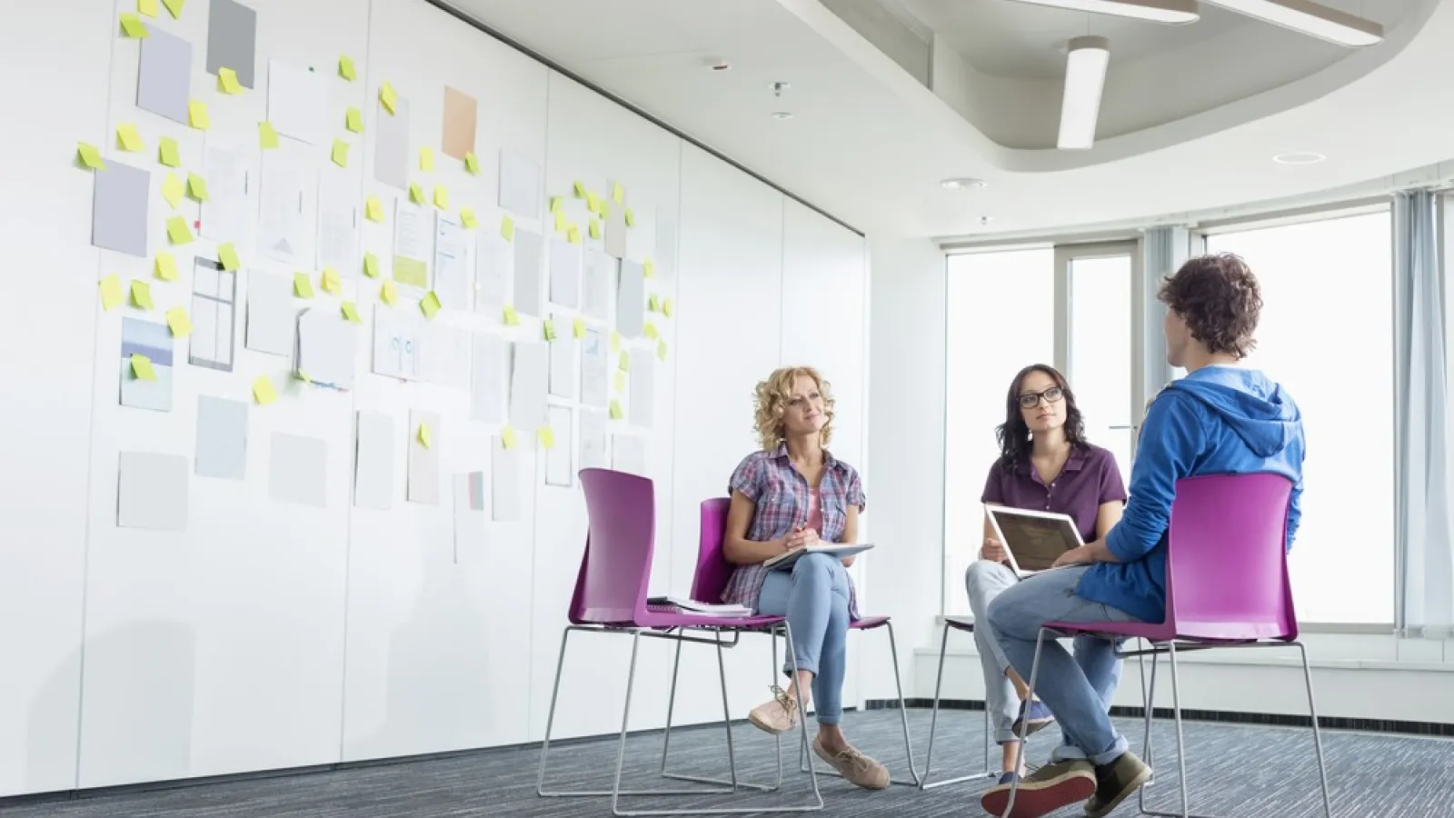 Three people having a chat inside a big white room 