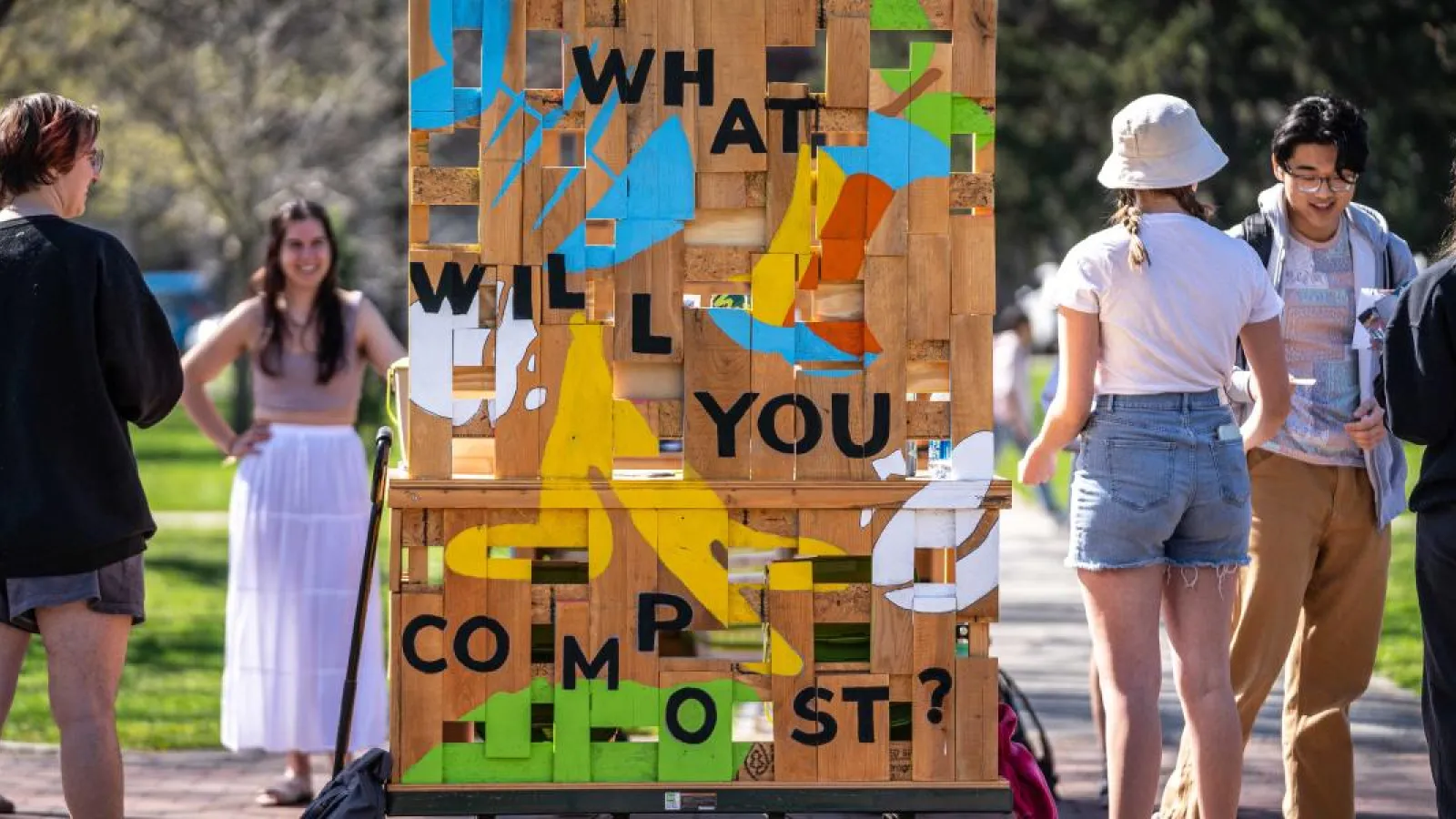 Group of students stand around a wagon that raises awareness about composting. Wagon is artfully designed with paint and words