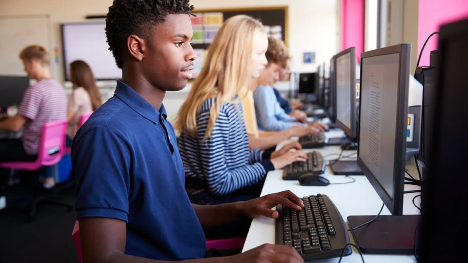 seven students are featured on screen using computers for word processing in a classroom setting
