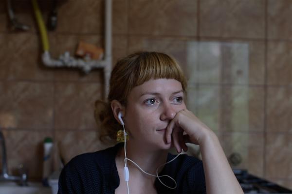 A women wearing earbuds with a saddened expression and thoughtful pose sits in a dark bathroom