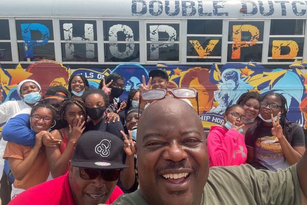 Dr. Will Patterson stands atop a crowd posing in front of the Hip Hop Xpress Double Dutch Boom Bus