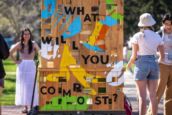 Group of students stand around a wagon that raises awareness about composting. Wagon is artfully designed with paint and words