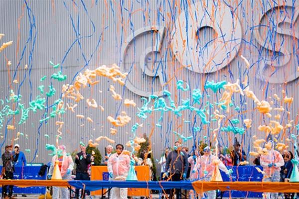 A number of colorful beakers erupt with slime into the air in front of the COSI building