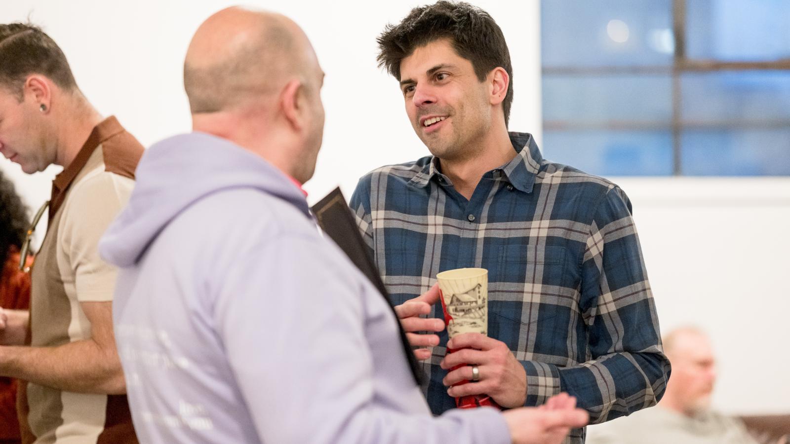 Two men talking, one smiling and the other with their back to the camera
